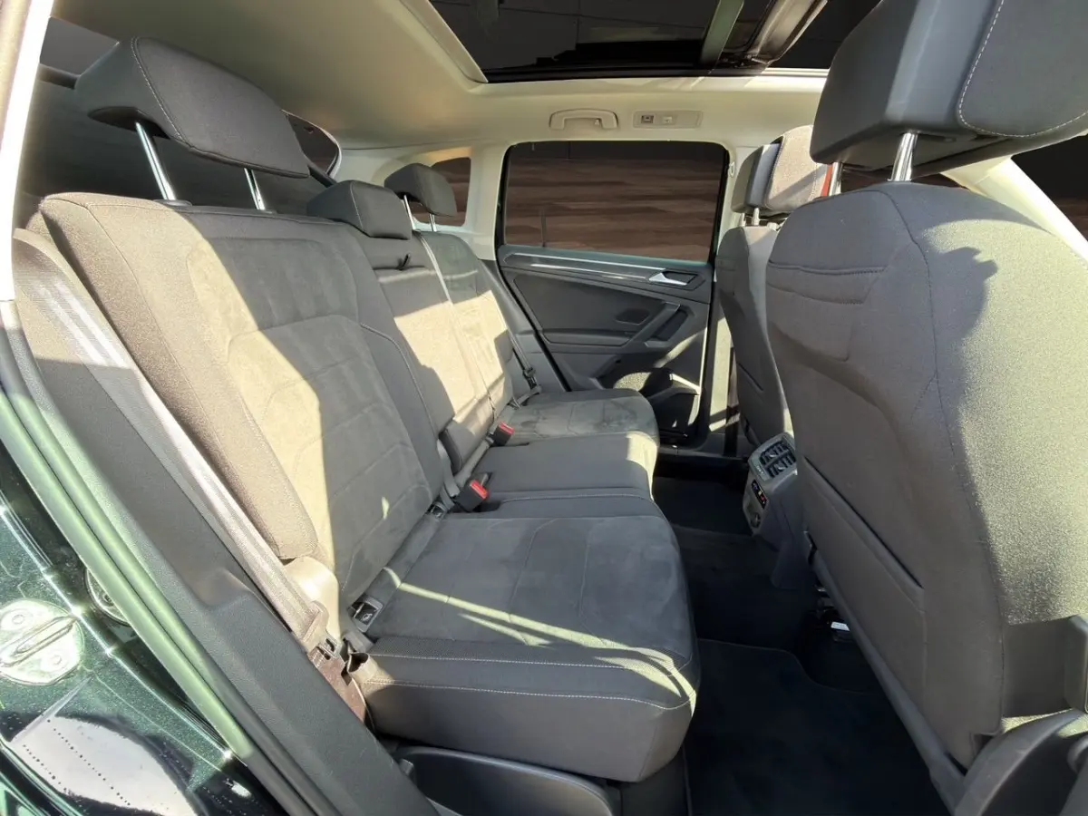 Vue intérieure arrière du Volkswagen Tiguan 2022 noir, sièges en tissu gris et toit ouvrant panoramique visible.