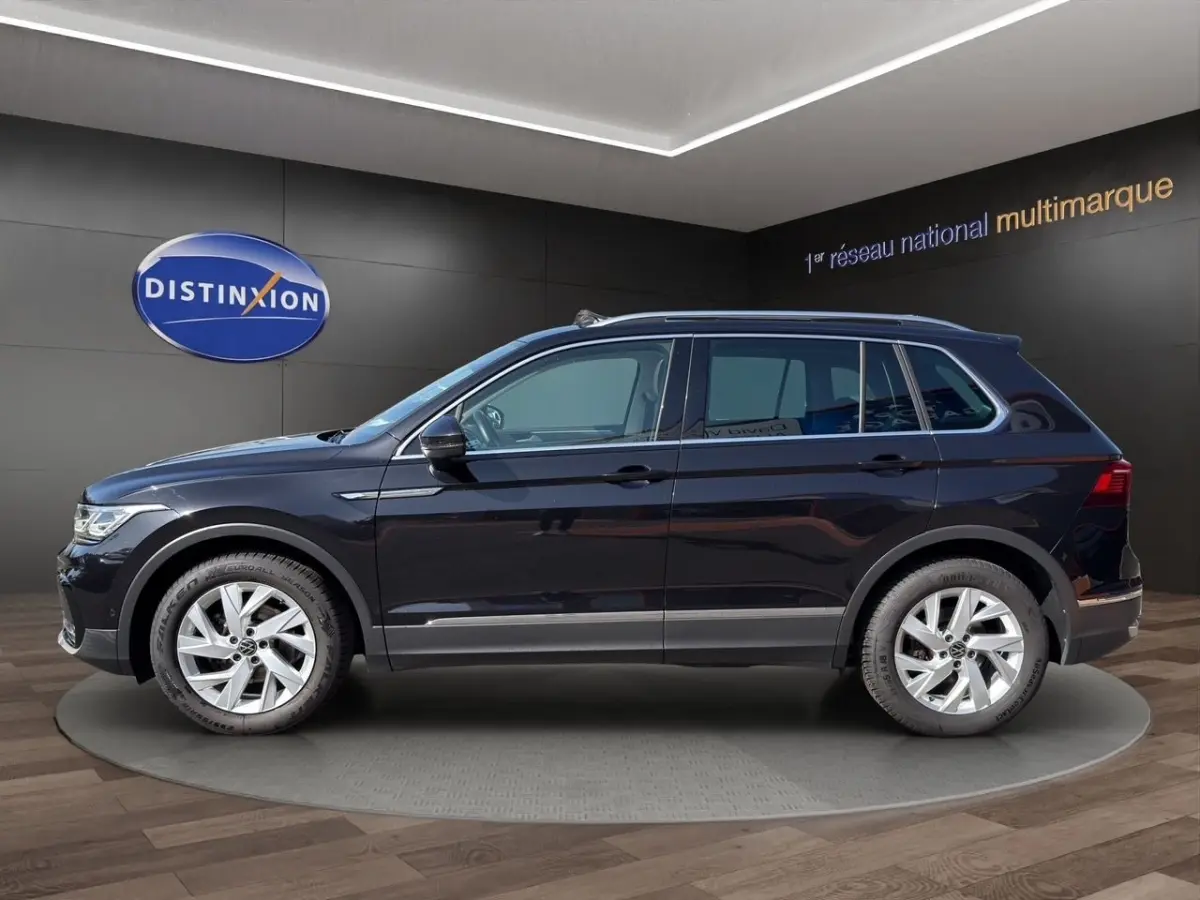 Profil droit d’un Volkswagen Tiguan noir 2022, finition Elegance, avec jantes alliage et barres de toit chromées.