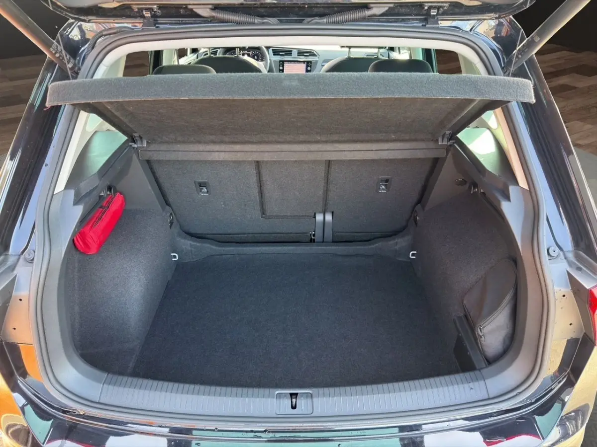 Coffre ouvert vu de l'arrière d'un Volkswagen Tiguan noir, avec tapis noir et rangement latéral rouge et noir.