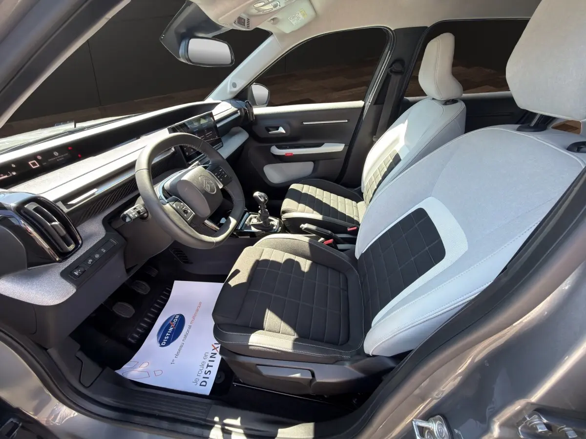Vue intérieure côté conducteur de la Citroën C3 2025 gris foncé, sièges bicolores et tableau de bord digital.