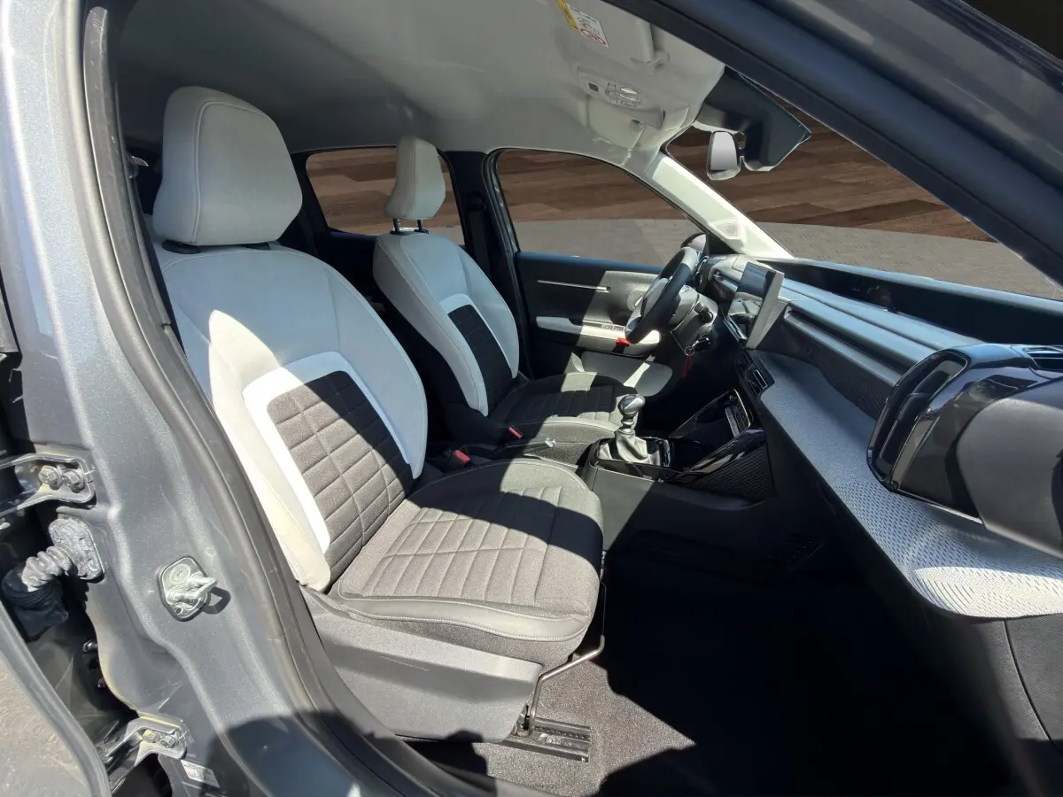 Intérieur avant droit de la Citroën C3 2025 gris foncé, sièges bi-ton gris clair et noir, tableau de bord moderne avec écran tactile.
