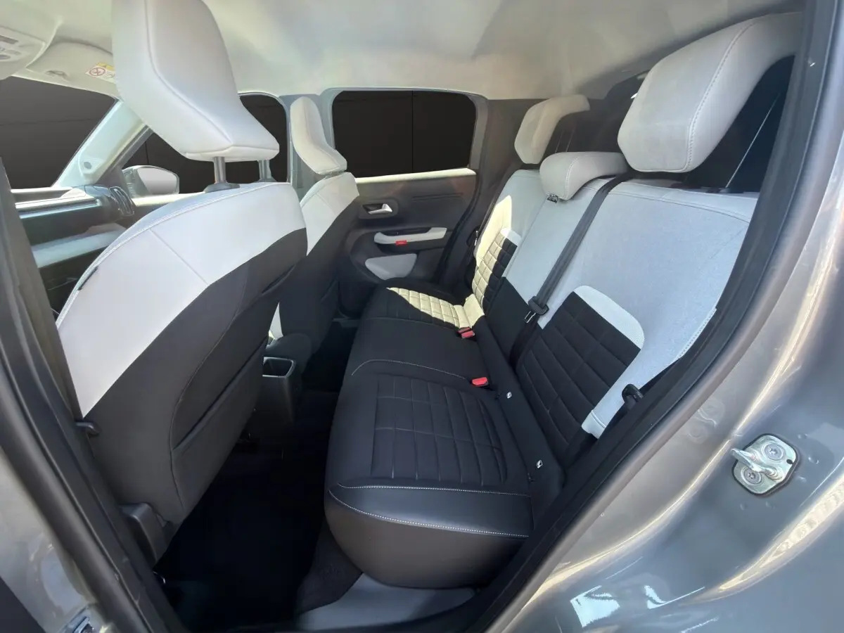 Vue intérieure arrière droite de la Citroën C3 2025 gris foncé, sièges bicolores noir et gris avec appuie-têtes intégrés.