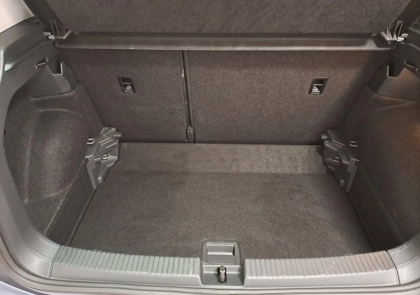 Vue intérieure du coffre spacieux et propre du Volkswagen T-Cross 2025 en gris cendré, avec revêtement textile noir.
