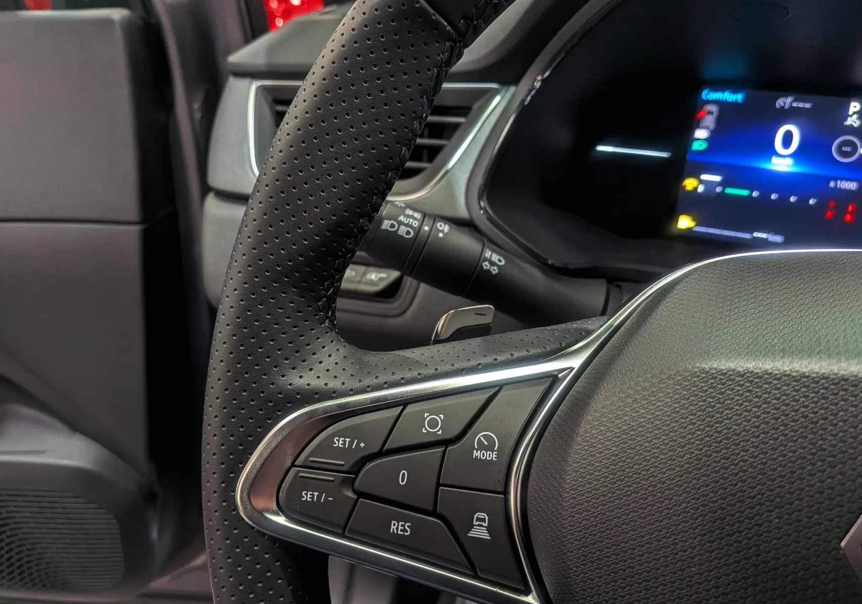 Gros plan sur le volant perforé du Renault Captur 2025, montrant les commandes de régulateur et l'écran numérique bleu du tableau de bord.