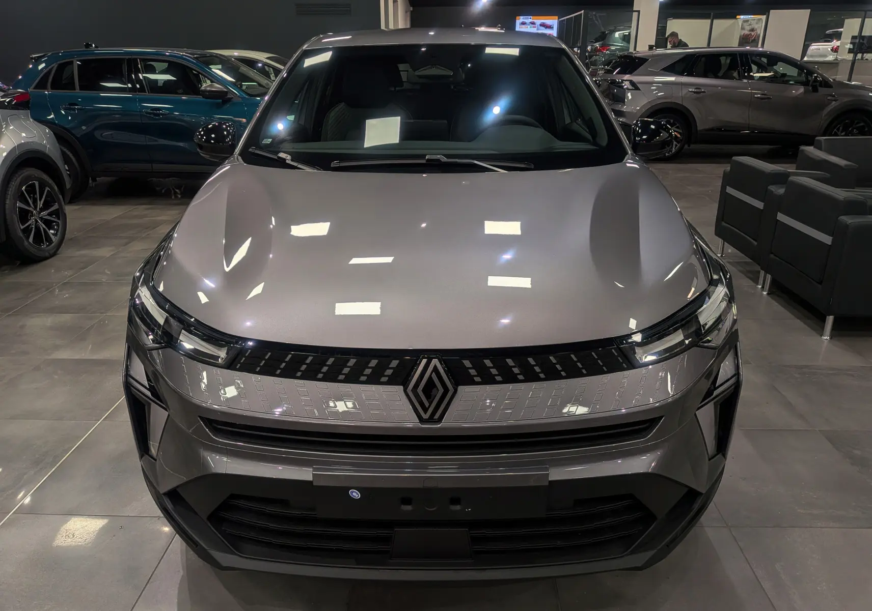 Vue frontale d'un Renault Captur 2025 gris Cassiopé avec calandre lumineuse et logo central dans un showroom.