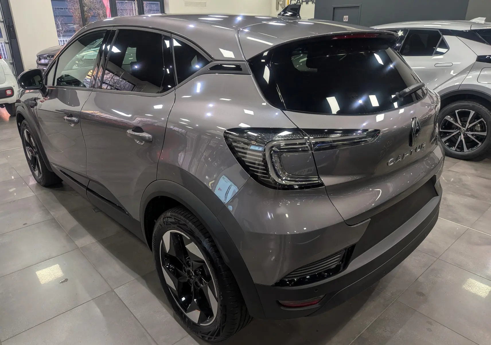 Vue 3/4 arrière droite du Renault Captur gris Cassiopé 2025 avec feux LED et jantes bi-ton noires en showroom.