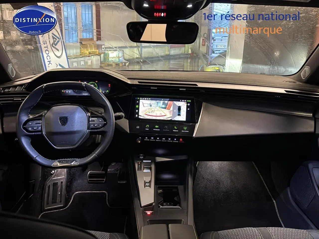 Vue intérieure avant de la Peugeot 408 Hybrid gris sellenium, avec tableau de bord numérique et écran tactile affichant la caméra de recul.