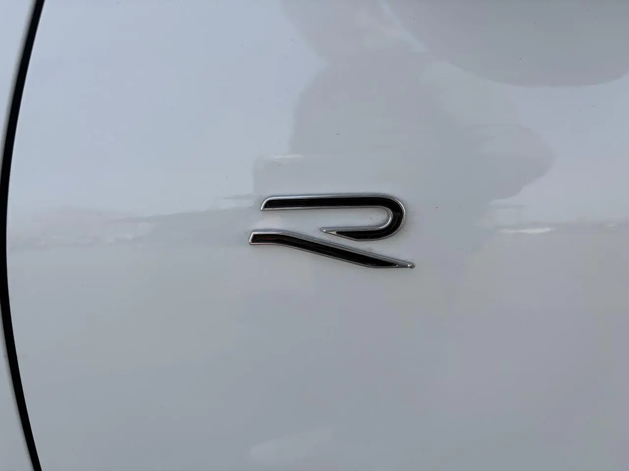 Gros plan sur l'emblème "R" chromé sur la porte blanche d'un Volkswagen T-Roc R-Line.