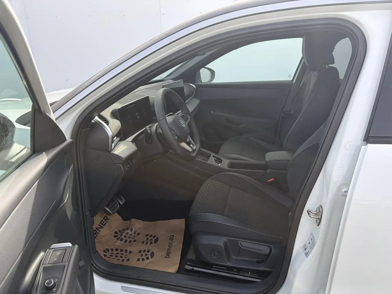 Vue intérieure côté gauche du Volkswagen T-Roc blanc pur, montrant les sièges sport noirs et le tableau de bord moderne.