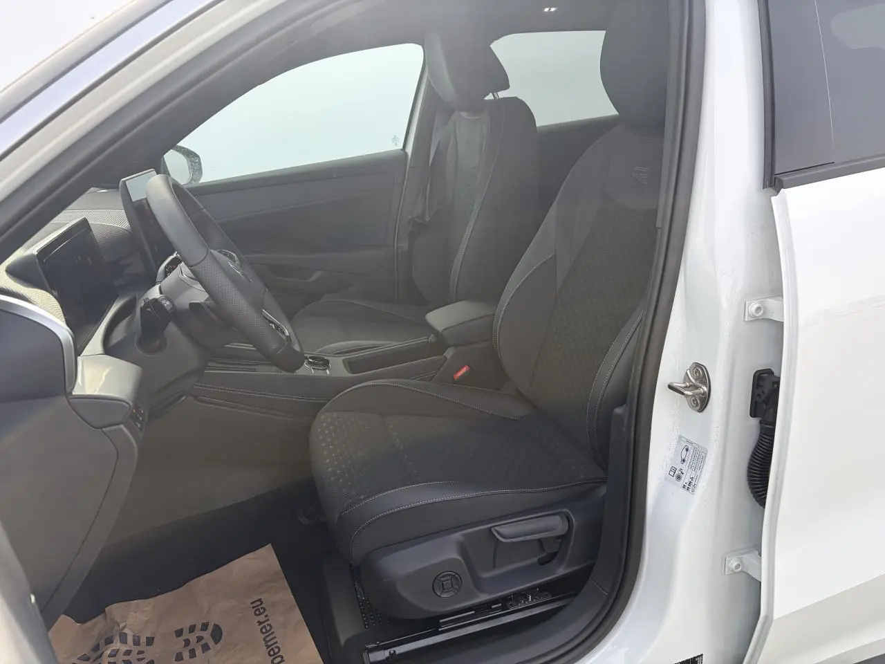 Vue intérieure côté conducteur du Volkswagen T-Roc blanc pur, montrant les sièges sport R-Line en tissu noir et le volant multifonction en cuir.