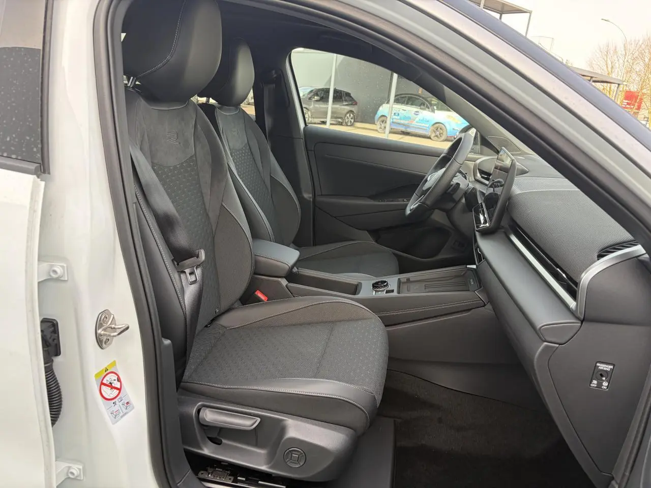 Vue intérieure côté conducteur du Volkswagen T-Roc blanc pur, mettant en valeur les sièges sport R-Line en tissu gris foncé.