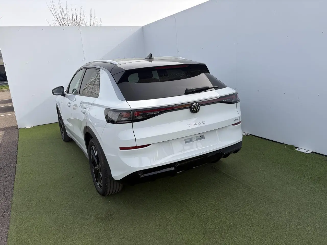 Vue 3/4 arrière droite du Volkswagen T-Roc blanc pur avec toit noir et feux arrière LED 3D sur fond neutre.