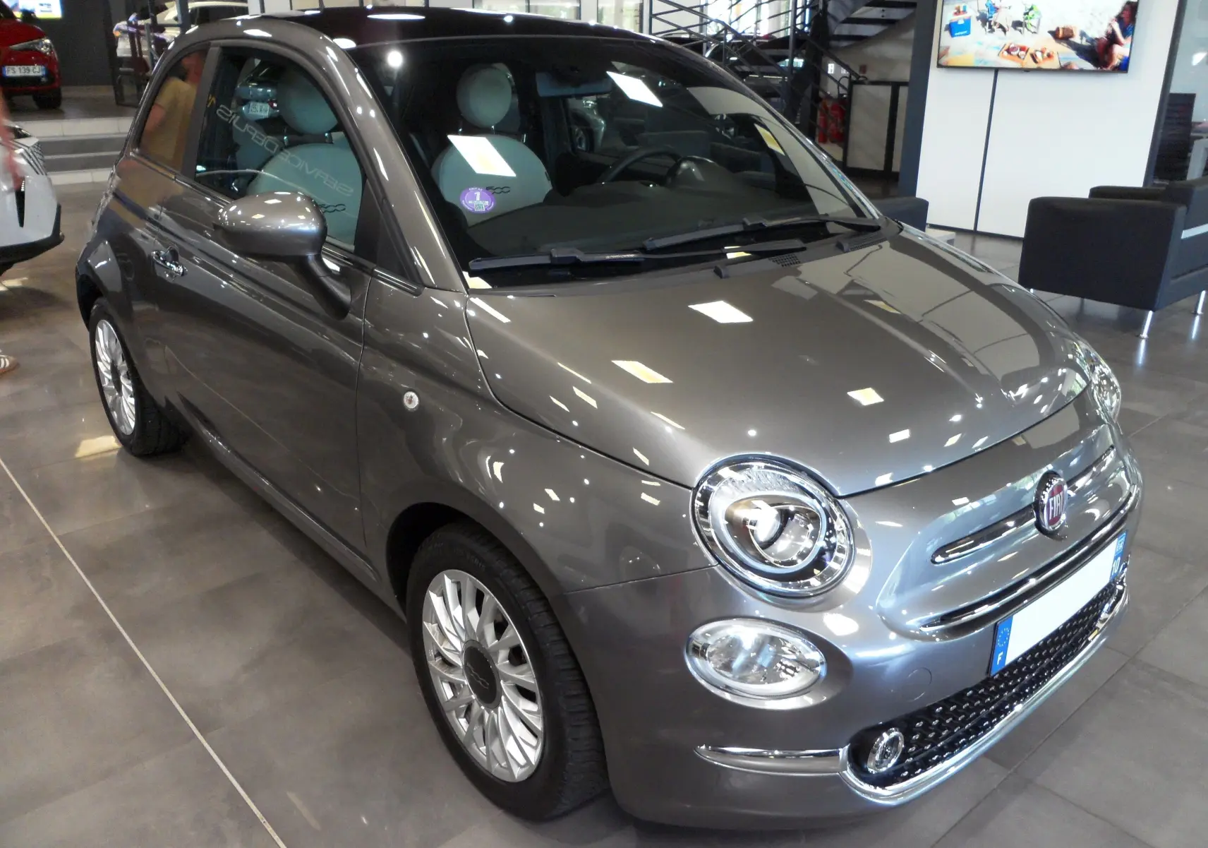 Vue 3/4 avant d'une FIAT 500 hybride 2021 gris Electroclash, avec phares ronds et jantes stylisées en concession.