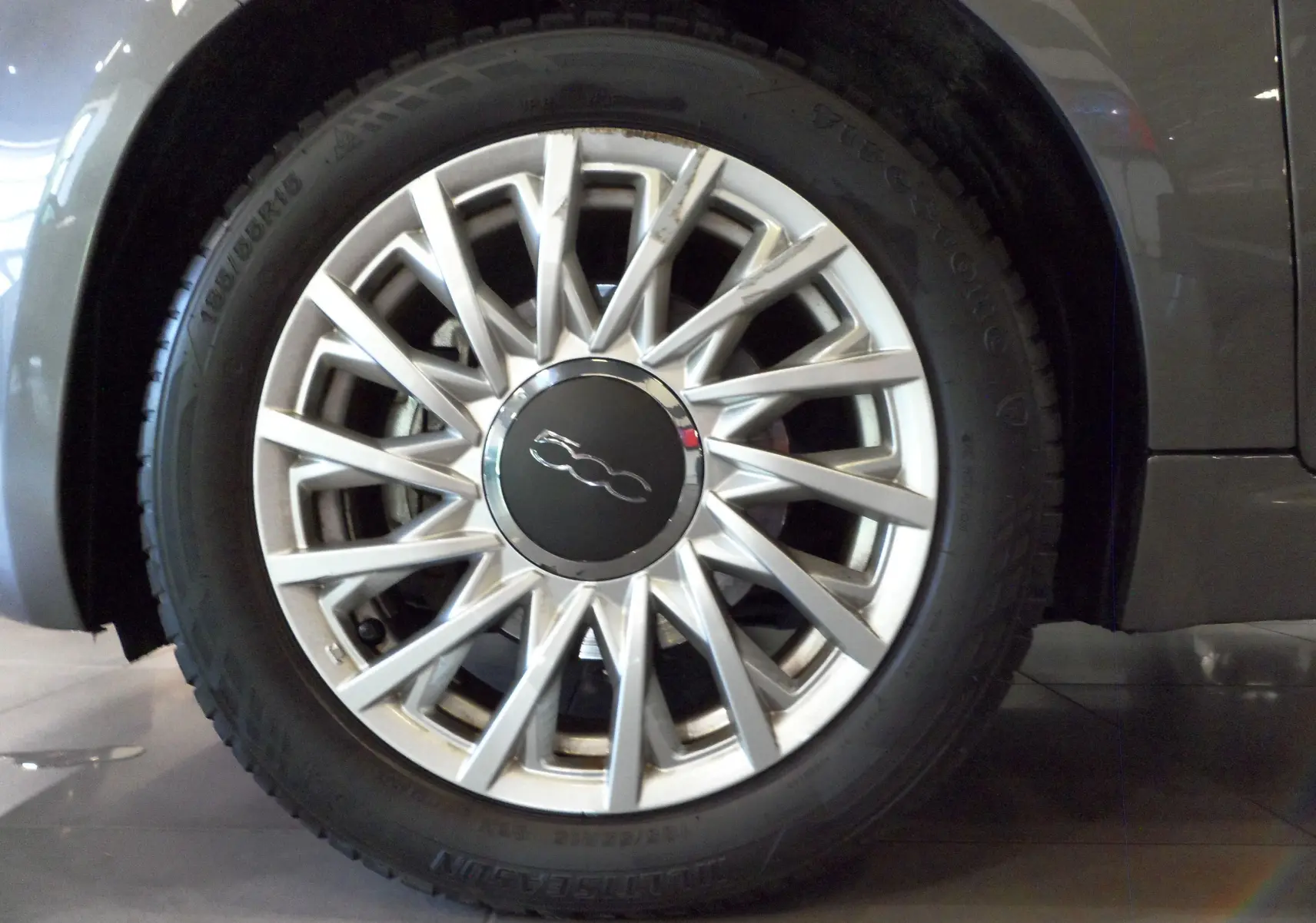 Gros plan sur la roue avant gauche d'une FIAT 500 Electroclash Grey, mettant en valeur la jante argentée au design étoilé.