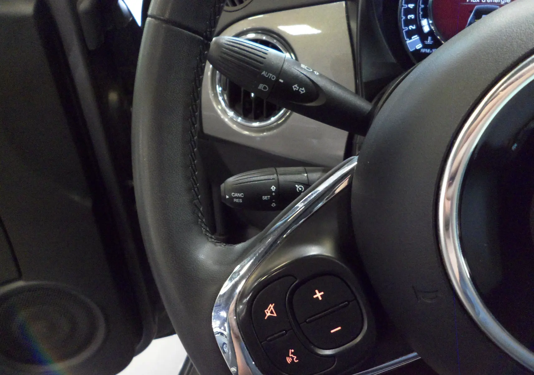 Gros plan sur le volant cuir noir de la Fiat 500 hybride 2021 avec commandes intégrées et aérateur gris Electroclash.