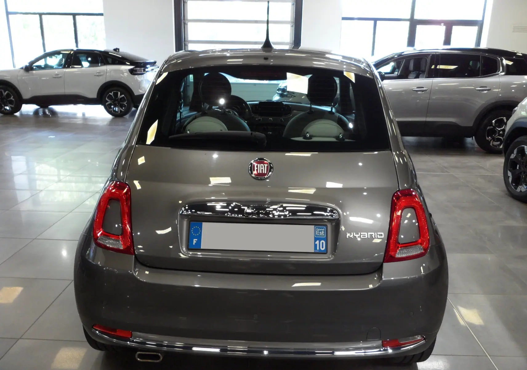 Vue arrière d'une Fiat 500 hybride Electroclash Grey exposée en showroom avec détails chromés et feux rouges.