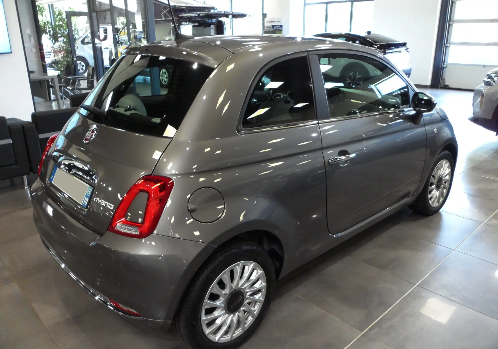 Vue 3/4 arrière droite d'une Fiat 500 Electroclash Grey hybride, soulignant ses feux arrière et jantes stylées en showroom.