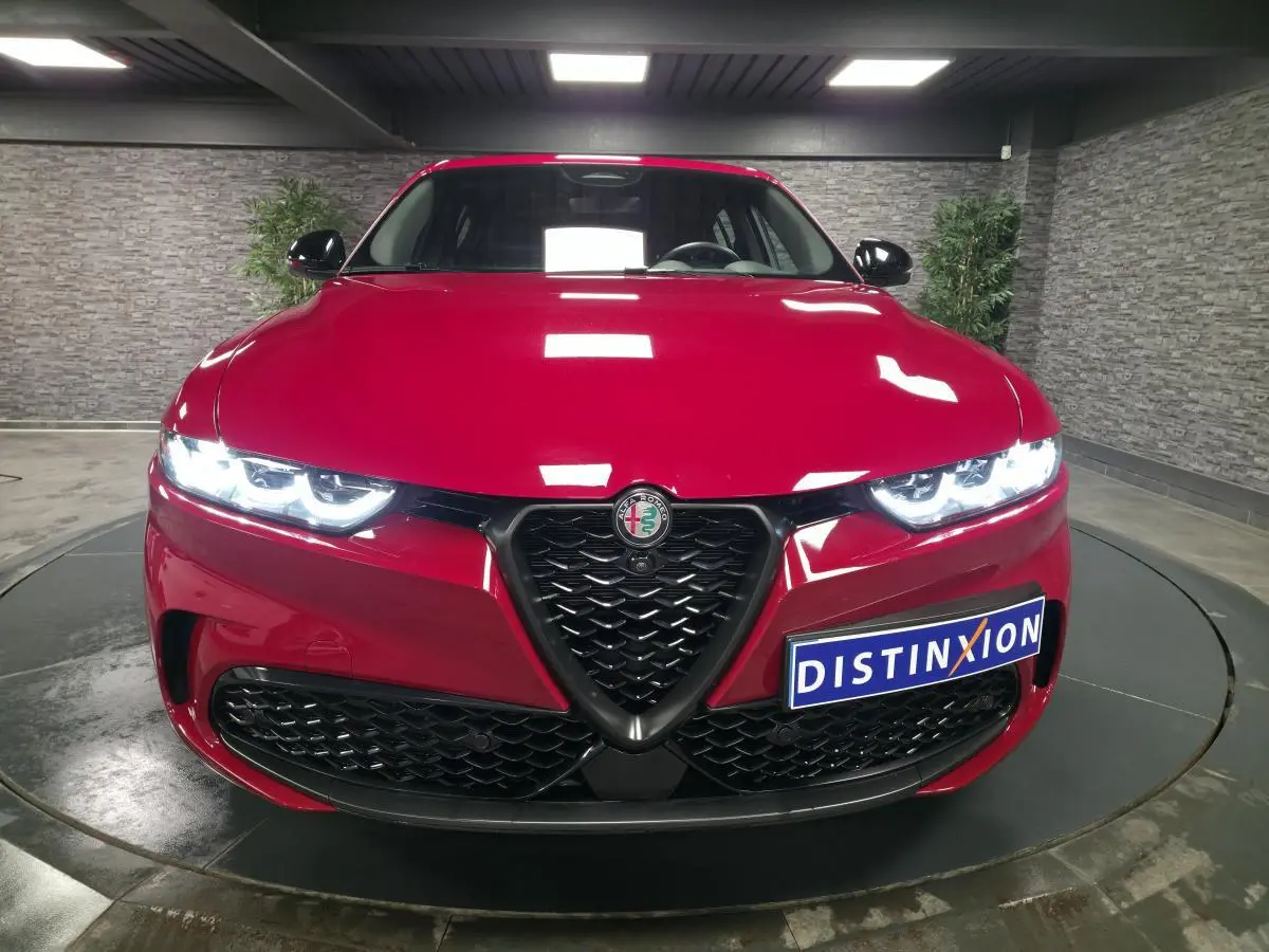 Vue frontale d'une Alfa Romeo Tonale rouge avec calandre noire et phares LED allumés dans un showroom.
