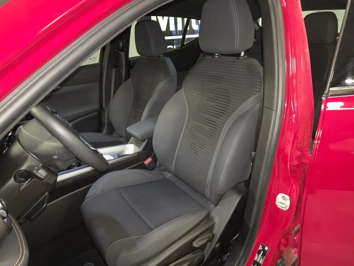 Vue intérieure côté conducteur de l'Alfa Romeo Tonale rouge 2025, sièges tissu noir avec surpiqûres beige et logo Biscione.