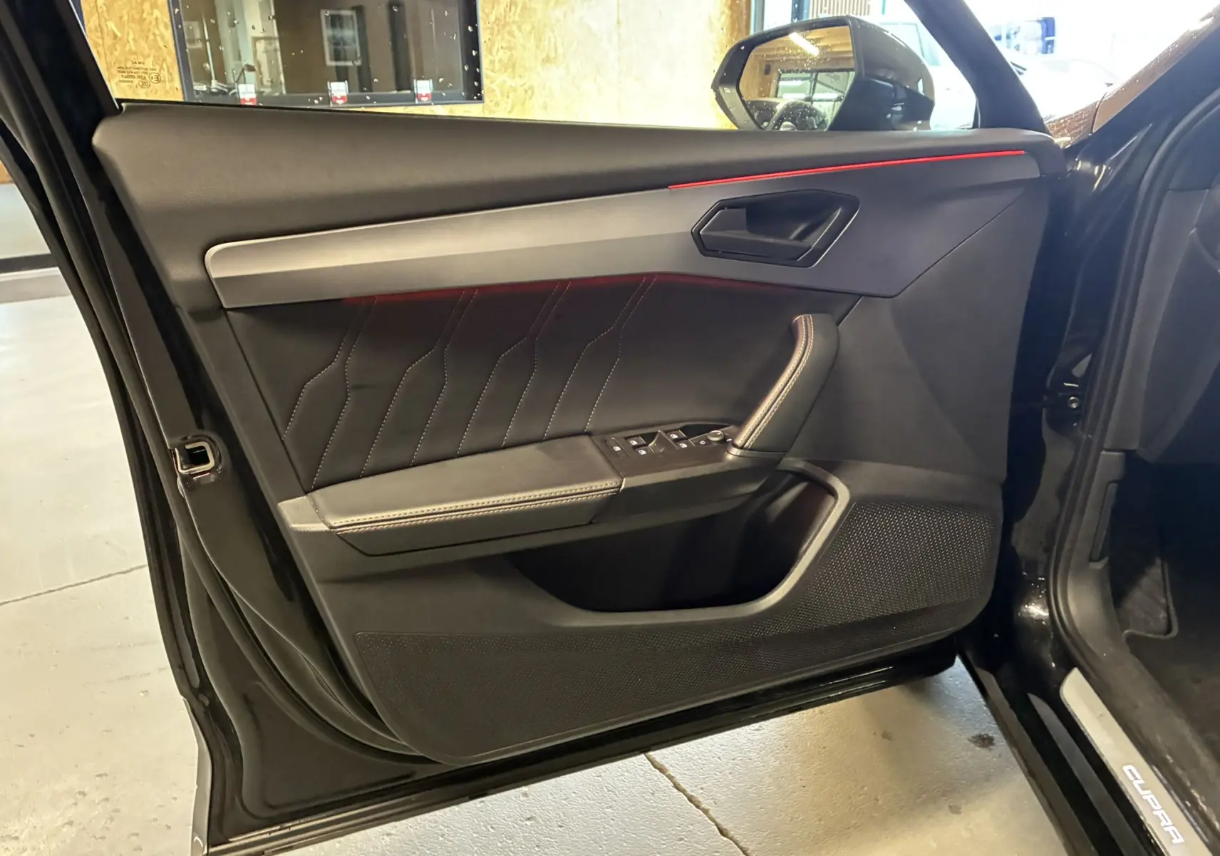 Vue intérieure côté gauche de la porte avant noire du CUPRA Formentor 1.4 E-HYBRID avec surpiqûres et bande rouge d’ambiance.