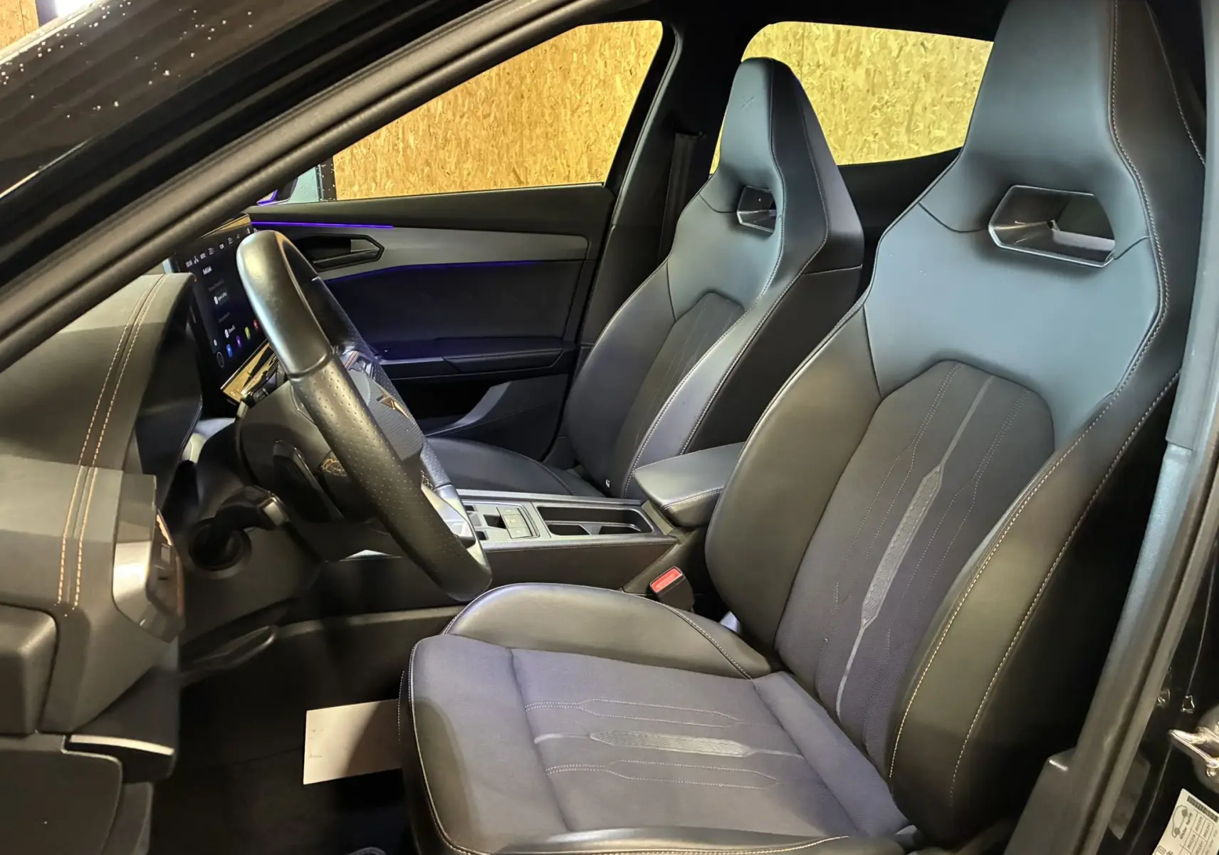 Vue intérieure côté conducteur de la CUPRA Formentor noire 2023, sièges sport en cuir et tissu avec surpiqûres contrastées.