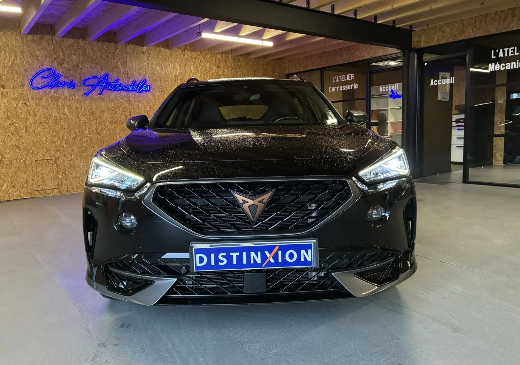 Vue avant d'une CUPRA Formentor noire 2023 avec calandre marquée et phares LED allumés en intérieur showroom.