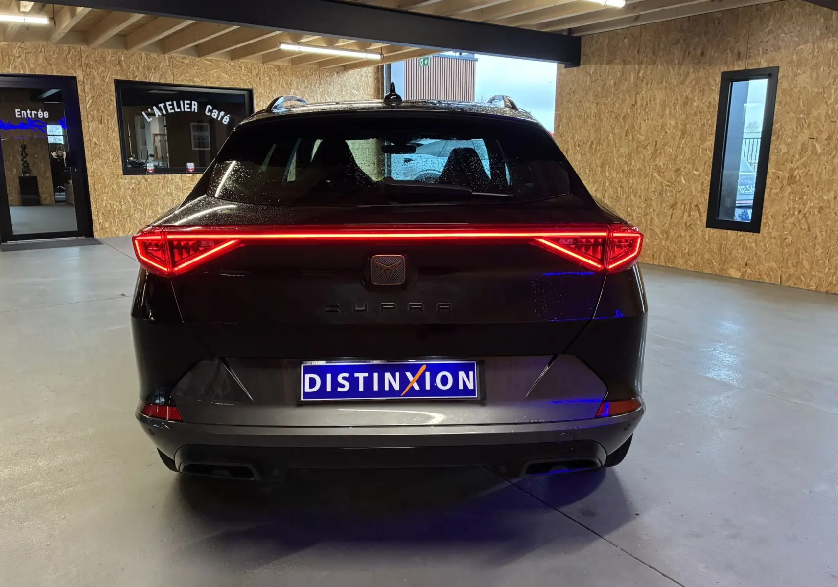 Vue arrière d’un CUPRA Formentor noir 2023 avec feux LED allumés, dans un garage lumineux avec murs en bois.