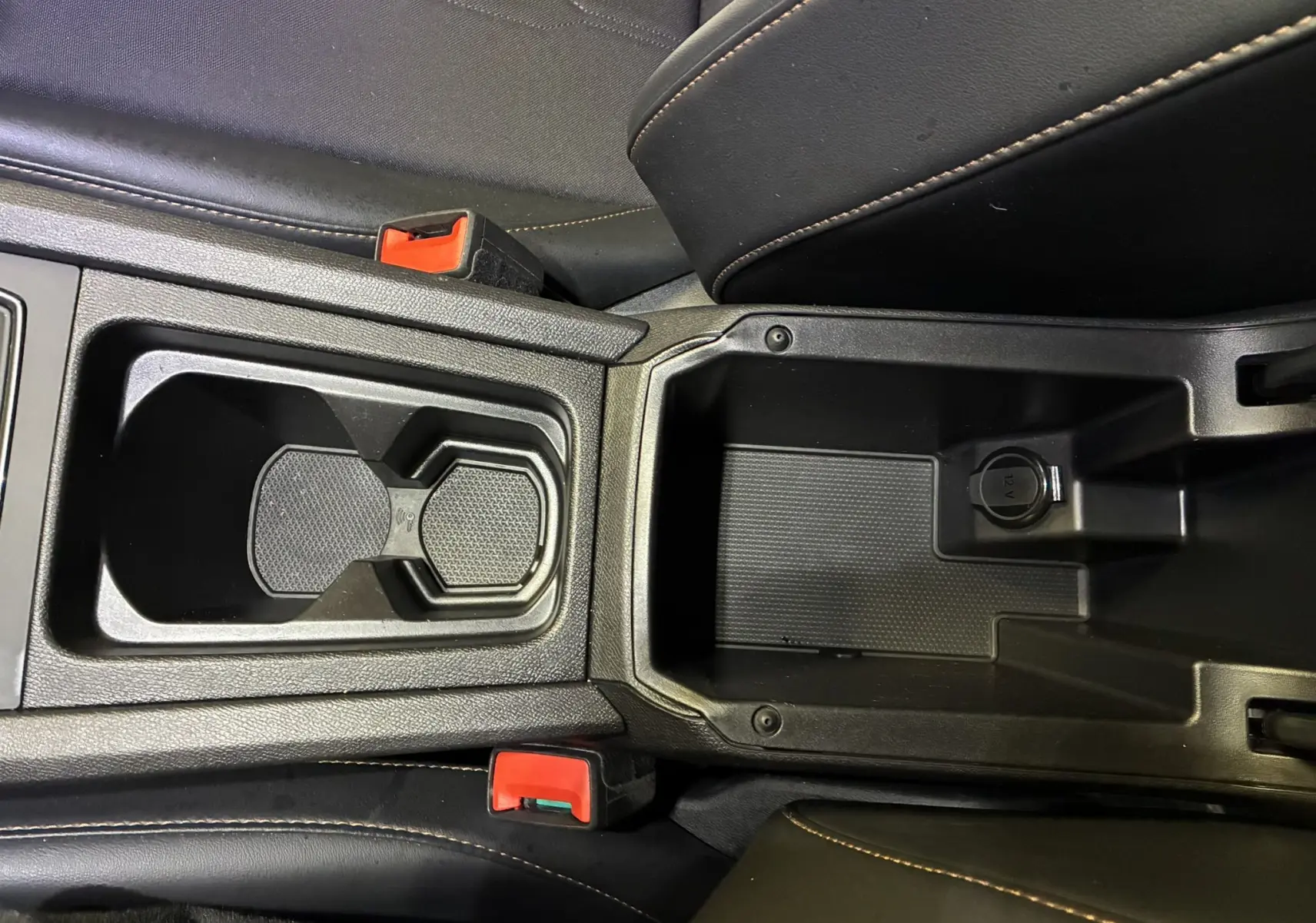 Vue rapprochée de la console centrale noire du CUPRA Formentor 1.4 E-HYBRID 2023 avec porte-gobelets et prise 12V.