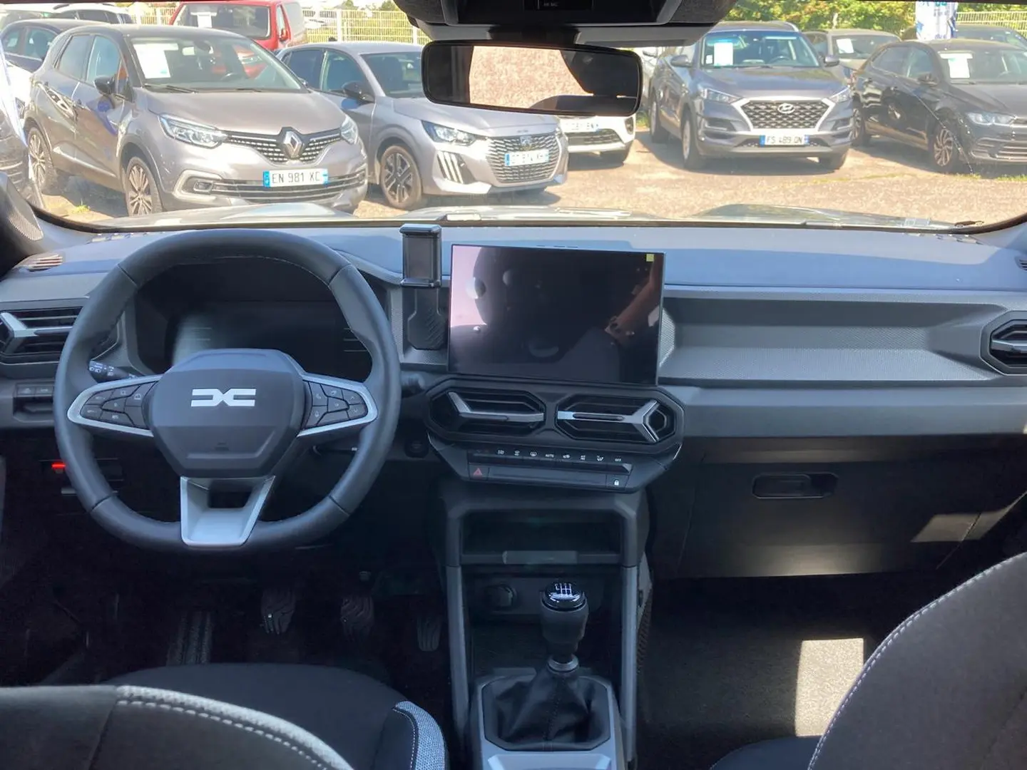 Vue intérieure avant du tableau de bord du Dacia Duster gris schiste 2026 avec volant multifonction et écran tactile central.