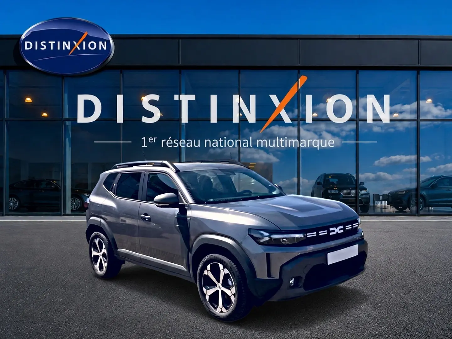 Vue 3/4 avant droit du Dacia Duster gris schiste 2026 avec jantes alu et barres de toit devant un showroom Distinxion.