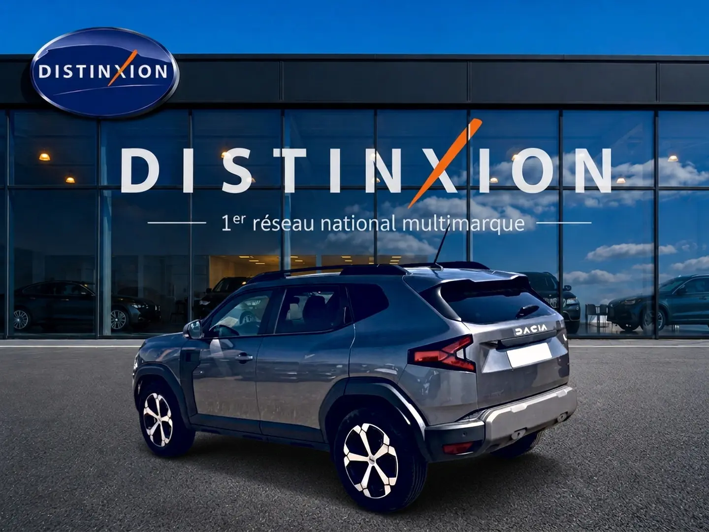 Vue 3/4 arrière droite du Dacia Duster gris schiste 2026 stationné devant une vitrine Distinxion.