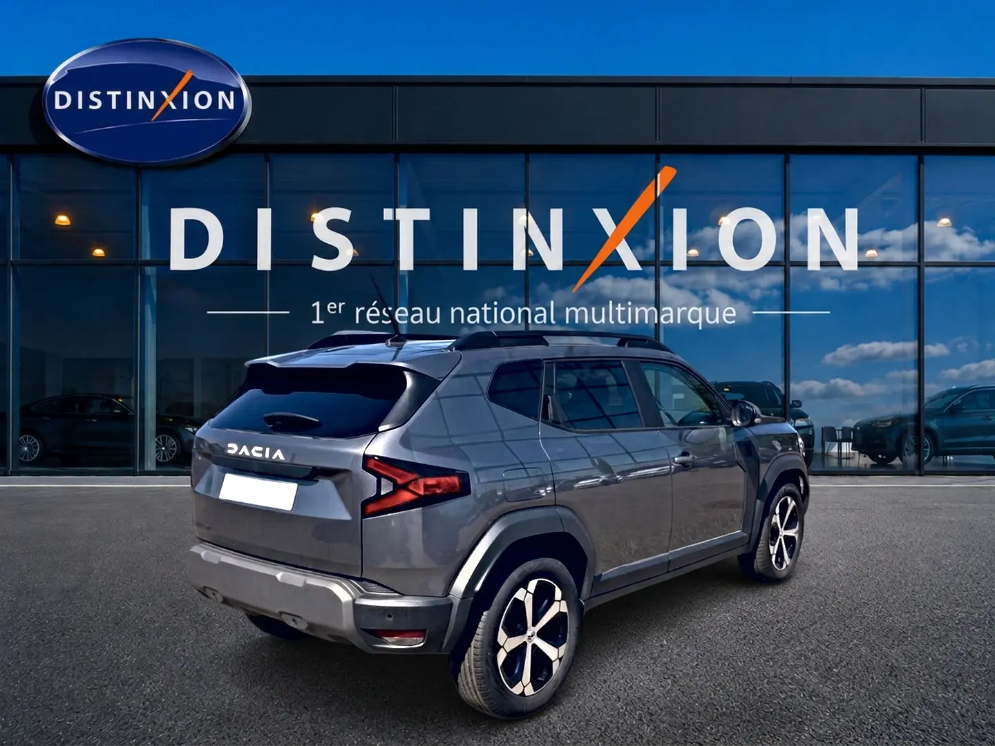 Vue 3/4 arrière droite d'un Dacia Duster gris schiste avec jantes alu, garé devant une vitrine Distinxion.