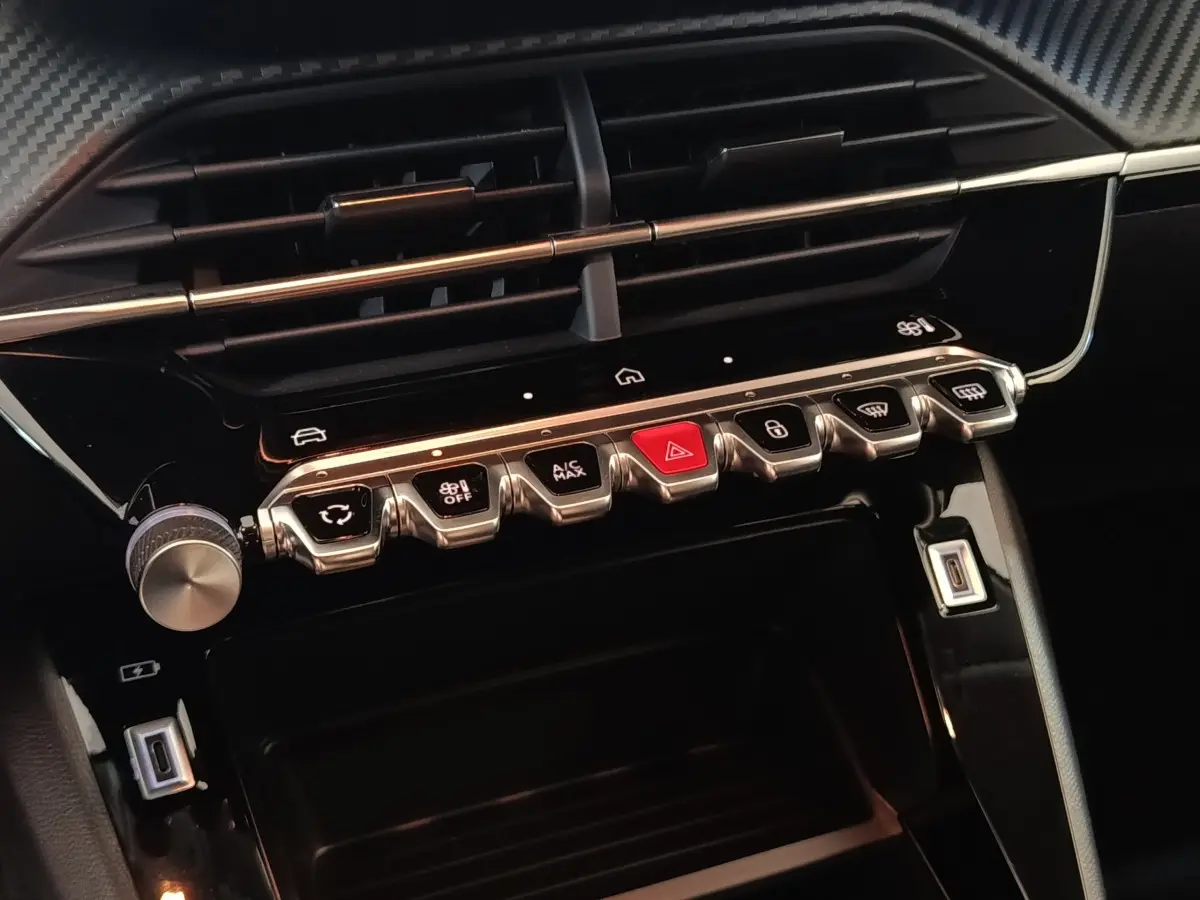 Gros plan sur la console centrale noire du Peugeot 208 Hybrid 2025, avec boutons de commande et prises USB visibles.