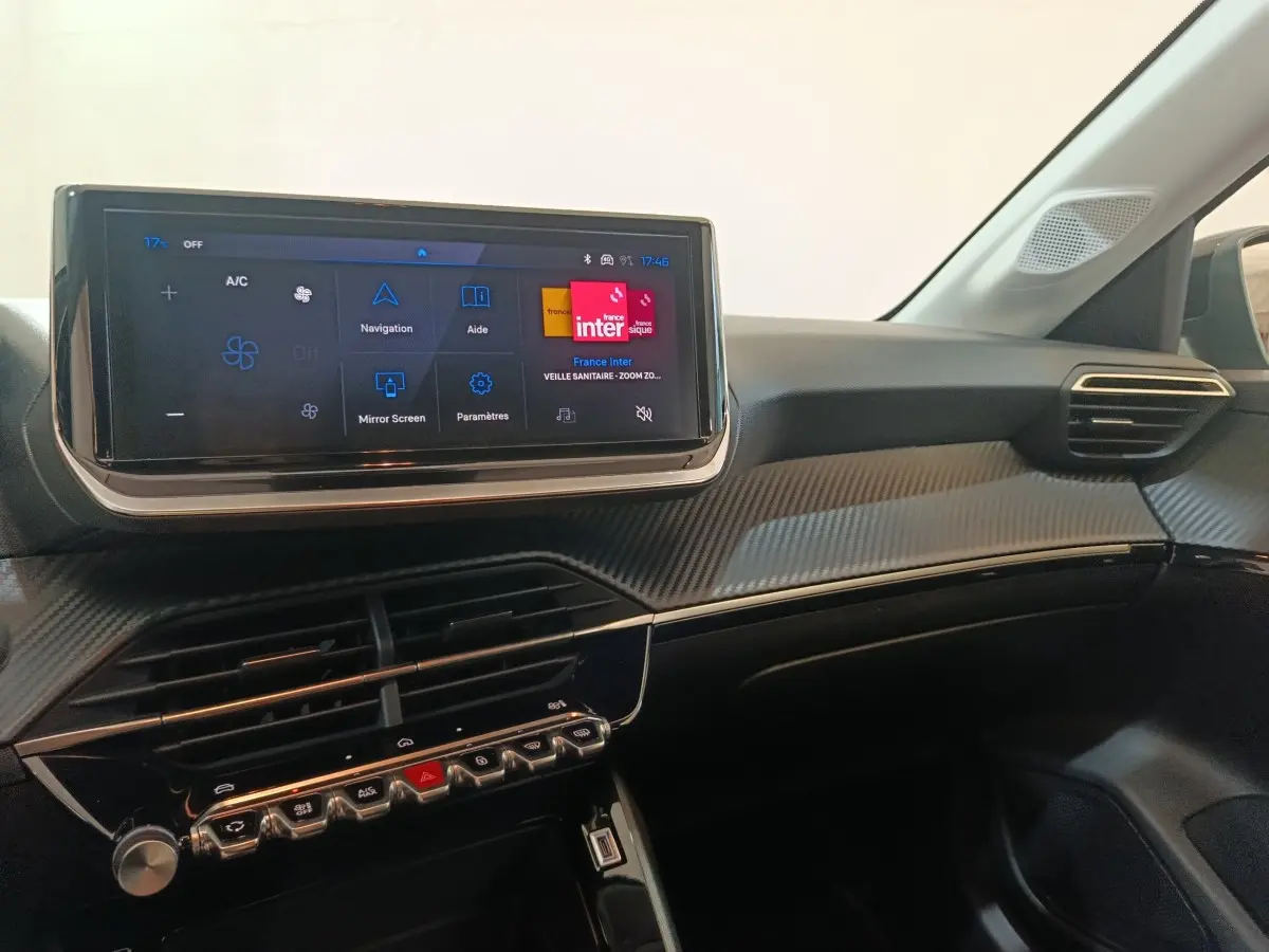 Vue intérieure du tableau de bord de la Peugeot 208 Hybrid 100 e-DCS6 Style 2025 avec écran tactile et finition carbone.