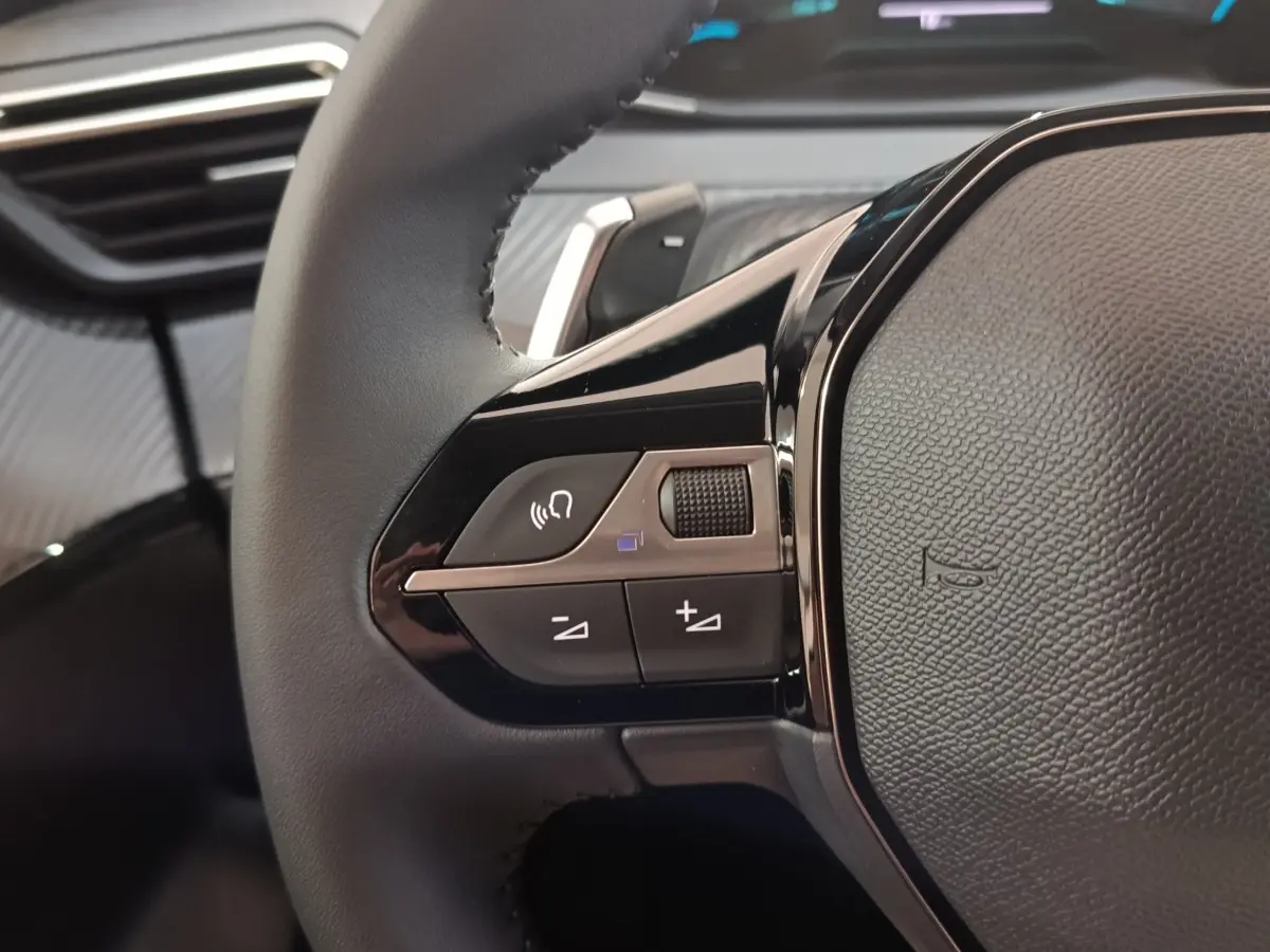 Gros plan sur le volant cuir noir de la Peugeot 208 Hybrid 2025, avec commandes multifonctions et finition brillante.