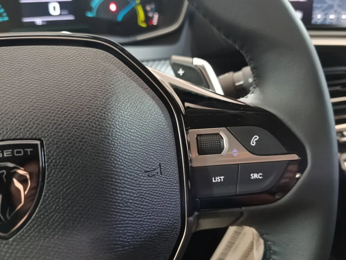 Gros plan sur le volant cuir noir de la Peugeot 208 Hybrid 2025, avec commandes multifonctions côté droit visibles.