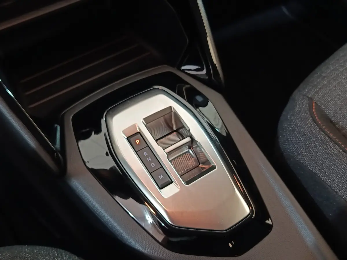 Gros plan sur la console centrale de la Peugeot 208 Hybrid 2025, avec levier de boîte automatique gris et noir.
