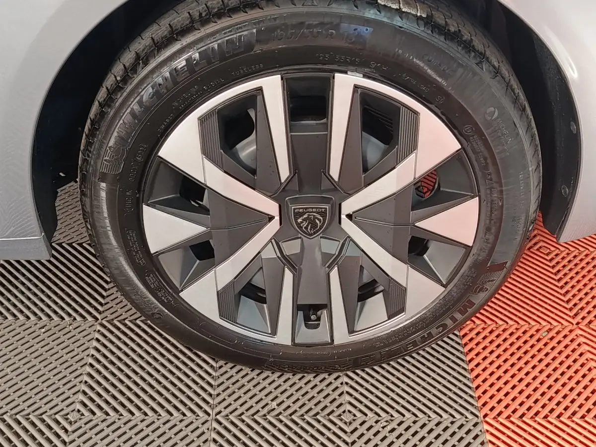 Gros plan sur la roue avant gauche avec jante stylisée bi-ton gris et noir de la Peugeot 208 Hybrid 2025 gris clair.