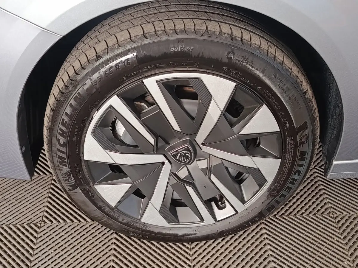 Gros plan sur la roue avant droite gris clair de la Peugeot 208 Hybrid 100 e-DCS6 avec jante en alliage au design géométrique.