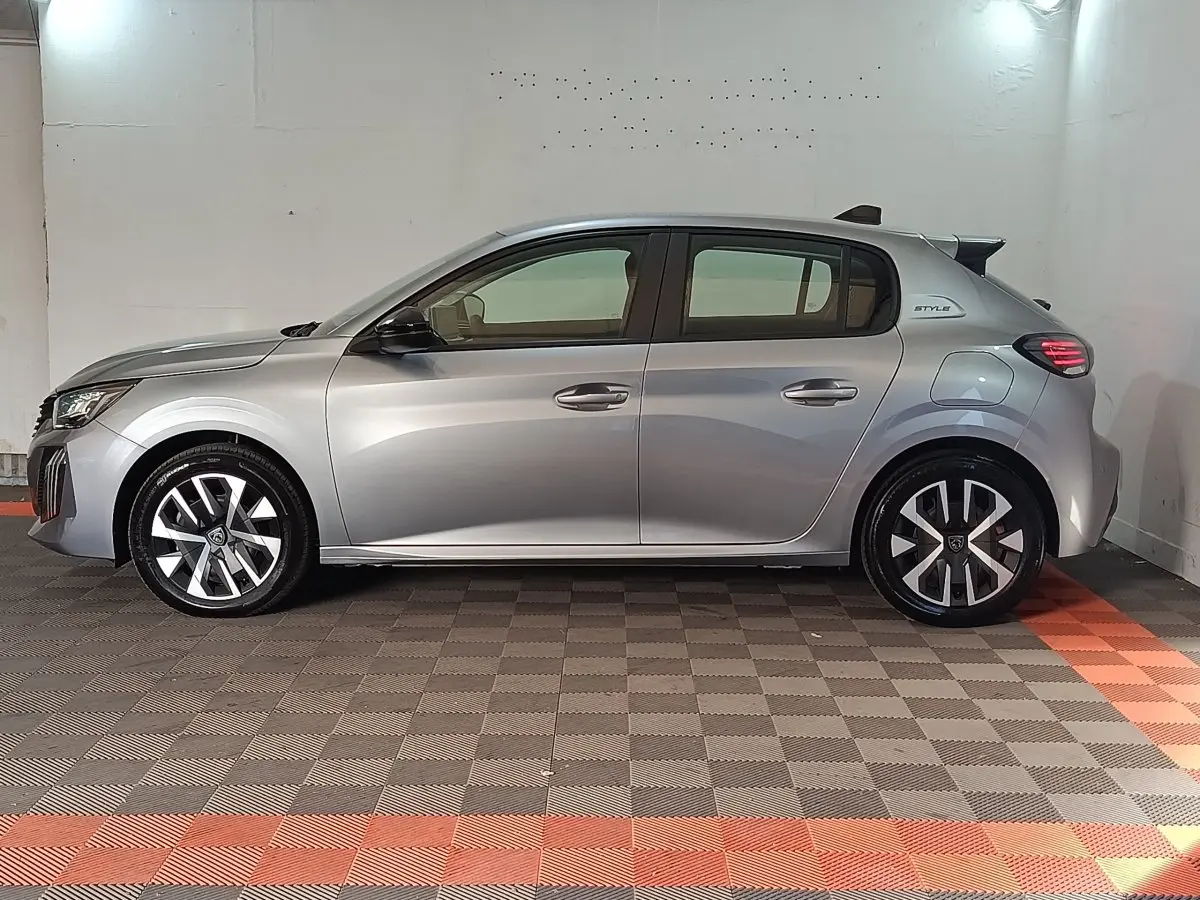 Profil latéral droit de la Peugeot 208 Hybrid gris clair 2025 avec jantes alliage et badge Style sur l'aile arrière.