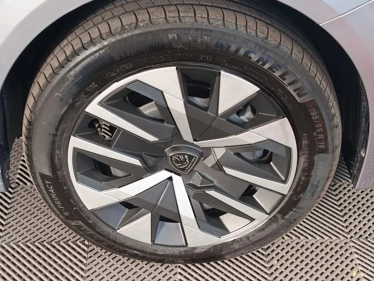 Gros plan sur la roue avant droite d'une Peugeot 208 Hybrid gris clair avec jante au design géométrique bicolore.