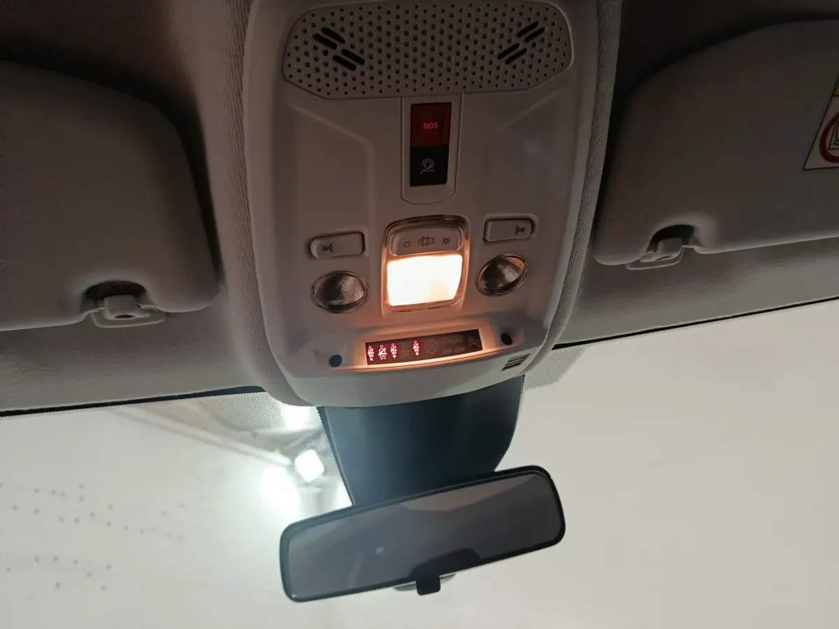 Vue intérieure du plafond avant de la Peugeot 208 Hybrid 100 e-DCS6 Style 2025 gris clair, avec plafonnier et rétroviseur central.