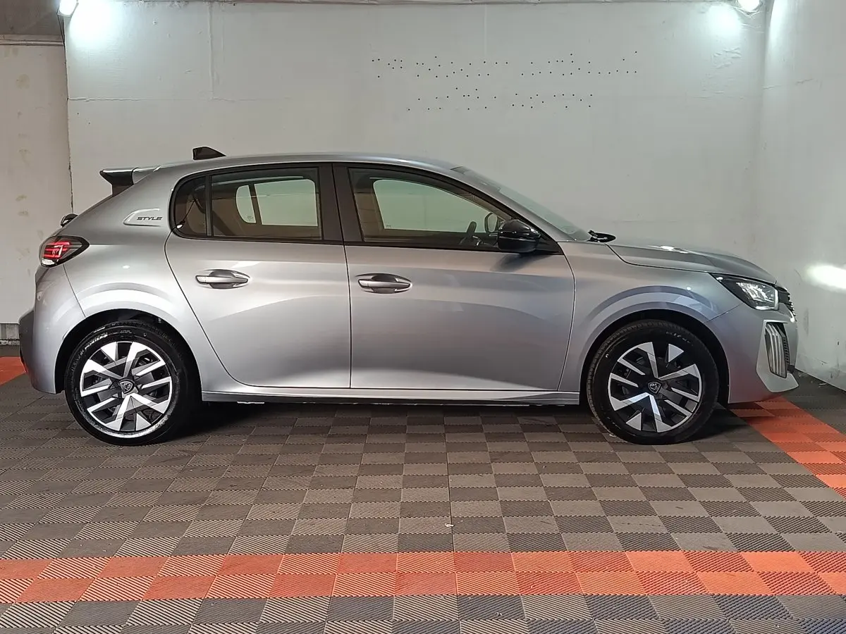 Profil droit d'une Peugeot 208 Hybrid gris clair 2025 avec jantes modernes et badge Style sur l'aile arrière.