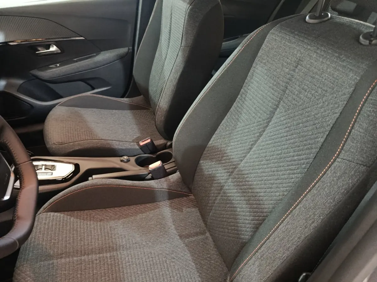 Vue intérieure rapprochée des sièges avant gris foncé avec surpiqûres orange de la Peugeot 208 Hybrid 2025.