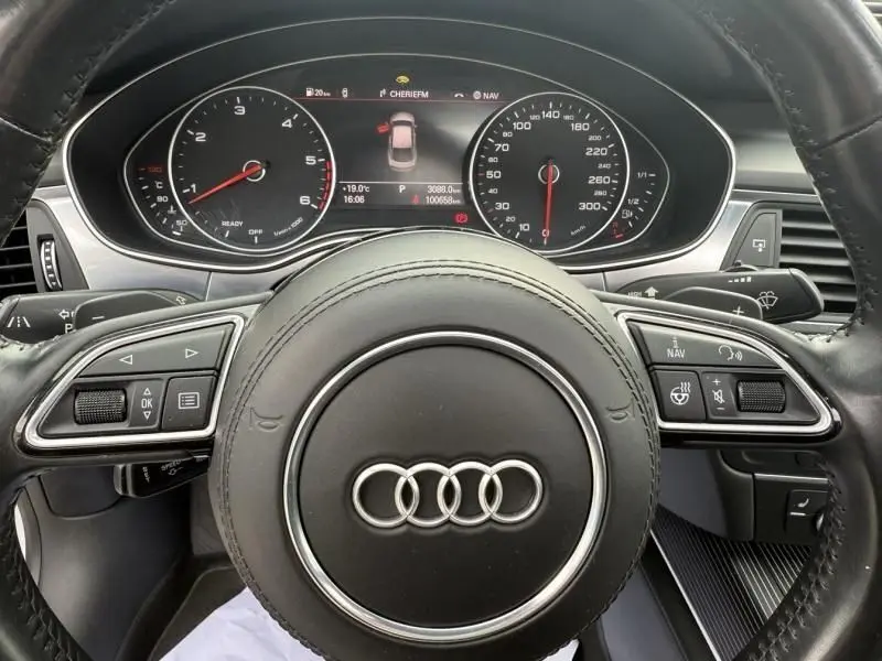 Vue rapprochée du tableau de bord et volant noir d'une Audi A7 Sportback blanche, affichage numérique et commandes intégrées.