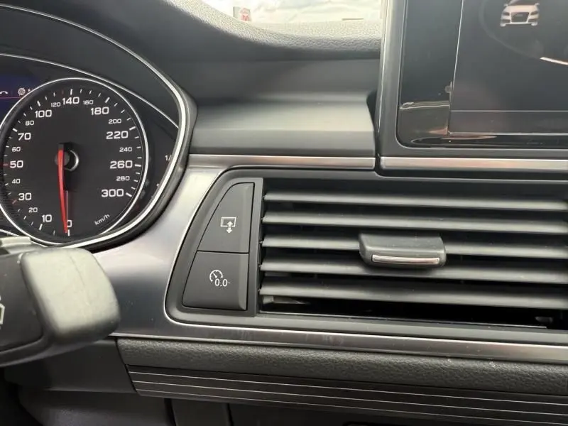 Détail du tableau de bord et de la console centrale d'une Audi A7 Sportback blanche, mettant en avant les aérateurs et le compteur.