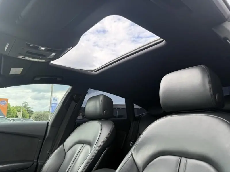 Intérieur de l'Audi A7 Sportback blanc 2018, vue côté conducteur montrant sièges cuir noirs et toit ouvrant panoramique.