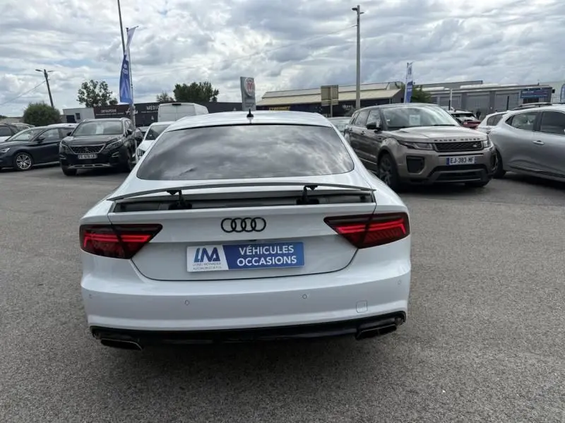 Vue arrière d'une Audi A7 Sportback blanche 2018 avec aileron déployé, stationnée sur un parking extérieur.