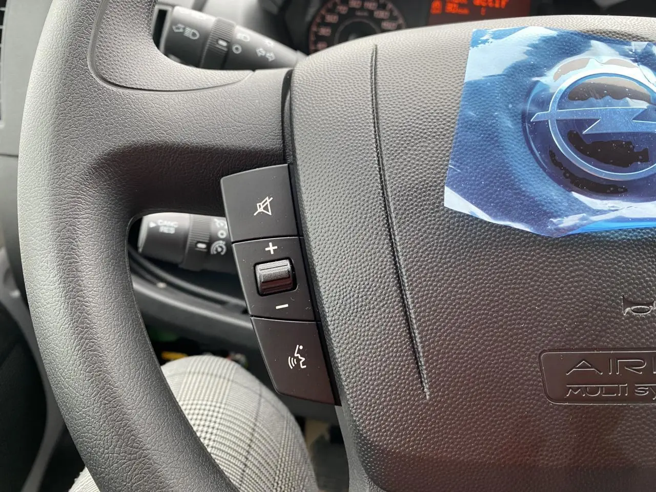Gros plan sur le volant noir de l'Opel Movano Fourgon 2022 avec commandes audio et logo protégé par un film bleu.