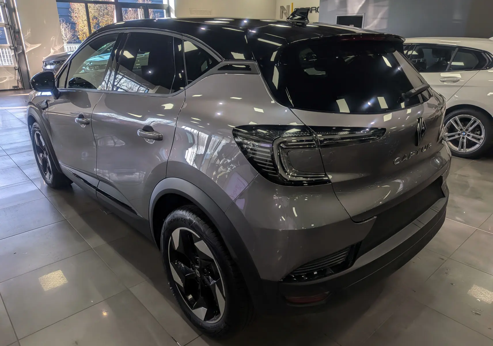 Renault Captur 2025 gris Cassiopé avec toit noir, vue 3/4 arrière droit en intérieur showroom.